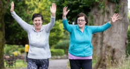 Two women in exercise clothes running and waving their arms in the air.